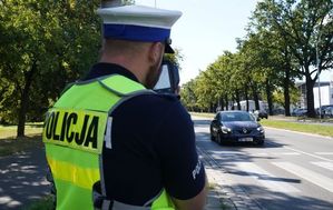 policjant stoi przy ulicy z mirnikiem prędkości w rękach, widać jadący pojazd