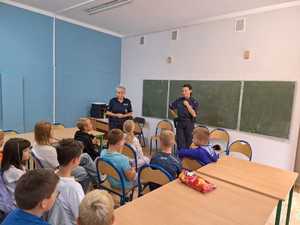 dwie policjantki stoją w klasie przy tablicy i rozmawiają a dziećmi, które siedzą na krzesłach