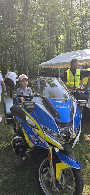 zdjęcie z festynu w plenerze, widać motocykl na pierwszym planie , dzieci i policjant