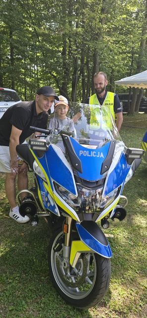 zdjęcie z festynu w plenerze, na motocyklu siedzi dziecko obok stoi mężczyzna