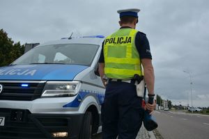 policjant stoi na poboczu drogi przyradiowozie