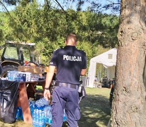 policjanci z woda idą w kierunku zabudowań , widać pojazdy