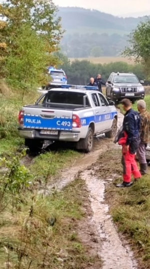 radiowóz jedzie po zabłoconej drodze widać inne pojazdy