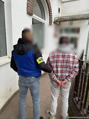 policjant prowadzi zatrzymanego mężczyznę , który ma założone z tyłu kajdanki