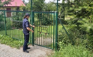 policjantka wchodzi na teren ogrodu działkowego, stoi przy furtce-ogrodzeniu