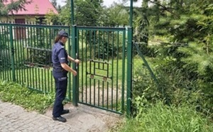 policjantka stoi przy wejściu do ogródków działkowych, w tle widać drzewa i krzaki