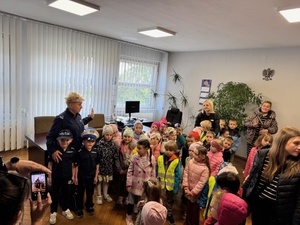grupa dzieci i policjant oraz policjantka stoją w pomieszczeniu policji