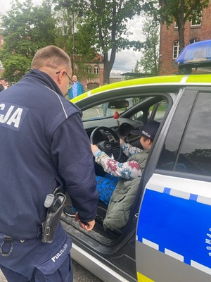 policjant stoi przy radiowozie  gdzie za kierowcą siedzi dziecko