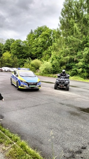 radiowóz im quad znajdują się na drodze , widać drzewa i drogę