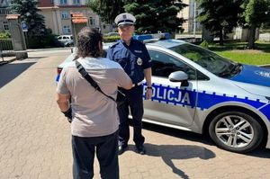 policjant przy radiowozie stoi przy mężczyźnie i podje mu rękę na parkingu