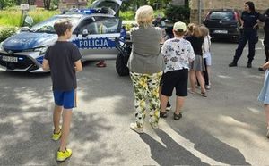 dzieci i kobieta stoją w pobliżu radiowozu policyjnego
