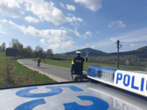 policjant stoi na drodze , widać rowerzystę jadącego i fragment radiowozu