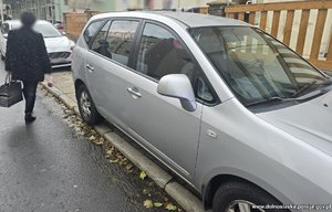 kobieta idzie ulica obok zaparkowanego na chodniku samochodu osobowego