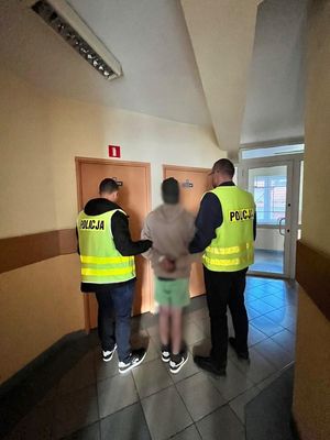 dwóch policjantów prowadzi zatrzymanego mężczyznę w pomieszczeniu jednostki policji