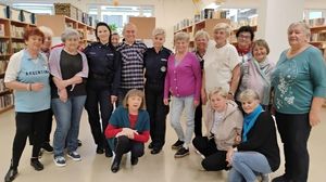 na zdjęciu dwie policjantki oraz grupa osób starszych w bibliotece, widać regały z książkami