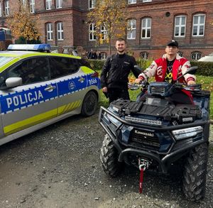 chłopiec siedzi na quadzie policyjnym obok  stoi policjant w tle widać budynek