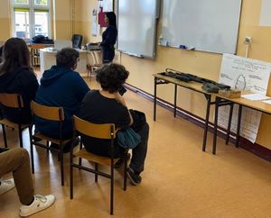 policjantka stoi przed uczniami siedzącymi na krzesłach  i prowadzi pogadankę w  sali lekcyjnej