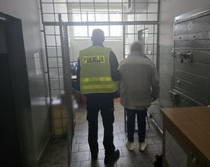 policjant prowadzi do pomieszczenia dla zatrzymanych okratowanego mężczyznę