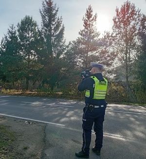 policjant stoi przy drodze i trzyma w reku urządzenie