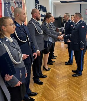 grupa policjantów w mundurach stoi w sali i przełożeni składają gratulacje