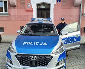policjant stoi przy radiowozie w tle budynek