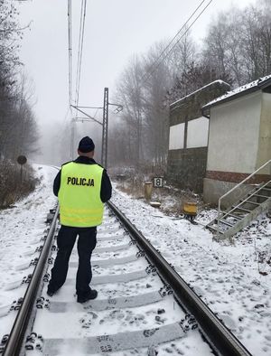 policjant stoi na torach , na ziemi leży śnieg, obok widac budynek