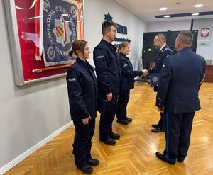 dwie policjantki i policjant stoją obok siebie w sali sztabowej a przełożeni składają gratulacje