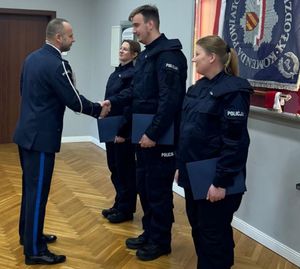 dwie policjantki i policjant stoją obok siebie w sali sztabowej a przełożony składa gratulacje