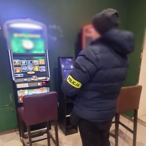 mężczyzna z opaska na rękawie z napisem Policja stoi przy automacie