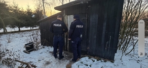 dwóch policjantów wchodzi do pustostanu-altany dookoła śnieg