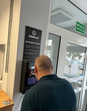 mężczyzna  stoi przy urządzeniu do badania stanu trzeźwości w pomieszczeniu policyjnym