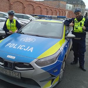 policjantka i policjant stoją przy radiowozie policyjnym w tle widać inne pojazdy