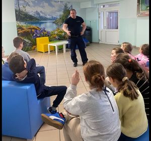 policjant stoji przy grupie dzieci , które siedzą na krzesełkach