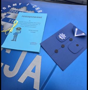 podziękowanie i laurka papierowa leżą na podkładzie z napisem policja