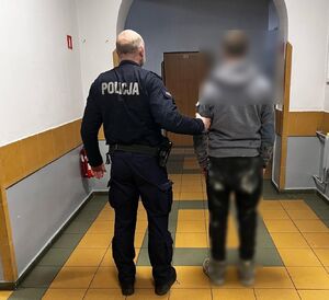 policjant prowadzi zatrzymanego mężczyznę  w pomieszczeniu służbowym policji