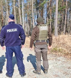 policjant i straz leśna stoją tyłem na terenei lesnym