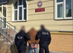 dwóch policjant.ow prowadzi mezczyzne do budynku komisariatu na którym widoczna jest tabliczk komisariat Policji w Kudowie -Zdroju i godło