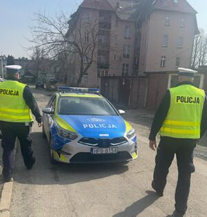 dwóch policjantów idzie w kierunku radiowozu policyjnego w tle widać budynek