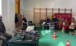 mundurowi stoją przy stolikach na których znajduje sie sprzęt służb. Zdjęcie wykonane w pomieszczeniu - sala sportowa