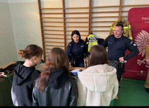 trzy dziewczyny stoją przy stoiku na którym jest prezentowany sprzęt mundurowych przy stoliku stoi policjantka i policjant oraz z boku siedzi kobieta