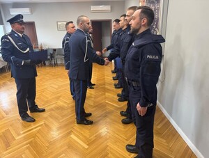 policjanci stoją w sali sztabowej policji ,a przełożony wręcza im dokument