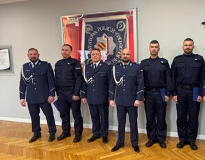 policjanci stoją w sali sztabowej przy sztandarze, który jest na ścianie w sali sztabowej