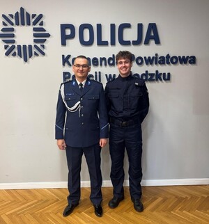 dwóch policjantów stoi w sali sztabowej przy sztandarze, który jest na ścianie w sali sztabowej