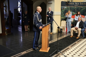 Komendant Powiatowy - policjant przemawia przy mównicy w sali zamkowej , na sali są policjanci i goście