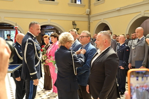 pani policjantka przypina odznaczenie  mężczyźnie w obecności Komendantów Policji , obok stoją inne osoby w sali zamkowej podczas uroczystości