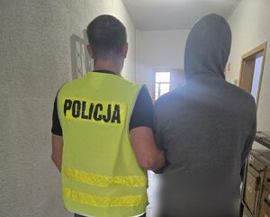 policjant prowadzi zatrzymanego mężczyznę, który ma kaptur na głowie