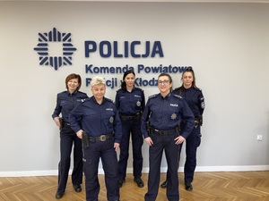 grupa policjantek i policjantów stoi obok siebie w sali sztabowej na ścianie napis Policja