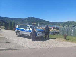 patrol policjantów stoi przy radiowozie policyjnym oznakowanym w pobliżu zbiornika wodnego