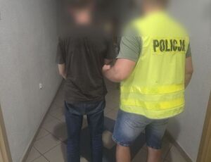 policjant z kamizelką  z napisem policja  prowadzi zatrzymanego mężczyznę