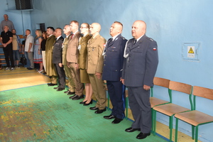 grupa mundurowych stoi obok siebie podczas uroczystości w tle widać młodzież